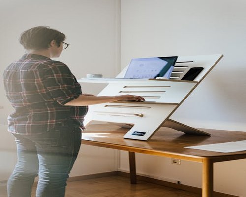 A bright home office workspace with a wooden desk, emphasizing regular standing breaks and ergonomic planning